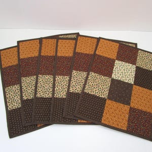 May include: Set of six brown and beige quilted placemats with a floral pattern. The placemats are made of fabric and have a square shape.