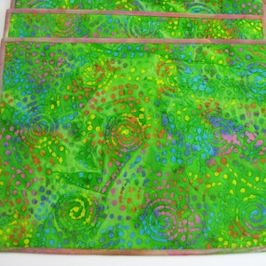 May include: Set of four green placemats with a colorful swirl and polka dot pattern. The placemats have a pink border.