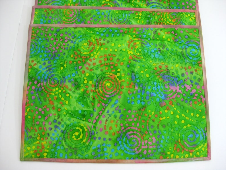 May include: Set of four green placemats with a colorful swirl and polka dot pattern. The placemats have a pink border.