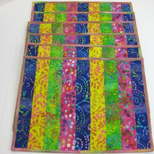 May include: Set of six colorful placemats with a striped pattern. The placemats are made of fabric and have a batik design. The colors are blue, green, yellow, and pink.
