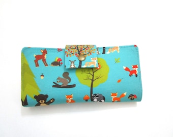 May include: A rectangular wallet with a teal background featuring a woodland scene. The design includes cartoon animals like deer, foxes, squirrels, and bears, along with trees and mushrooms. The wallet has a button closure.