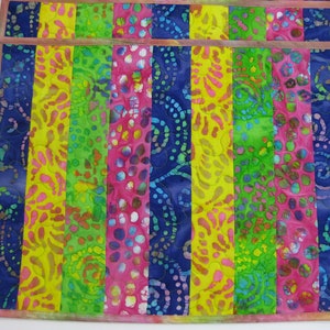 May include: Set of two colorful placemats with a striped pattern in shades of blue, green, yellow, and pink. The fabric has a batik design with swirls and dots.