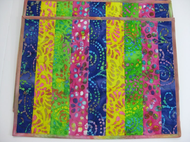 May include: Set of two colorful placemats with a striped pattern in shades of blue, green, yellow, and pink. The fabric has a batik design with swirls and dots.