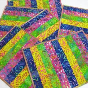 May include: Set of six colorful placemats with a striped pattern in shades of pink, yellow, green, and blue. The placemats are made of fabric with a batik design.