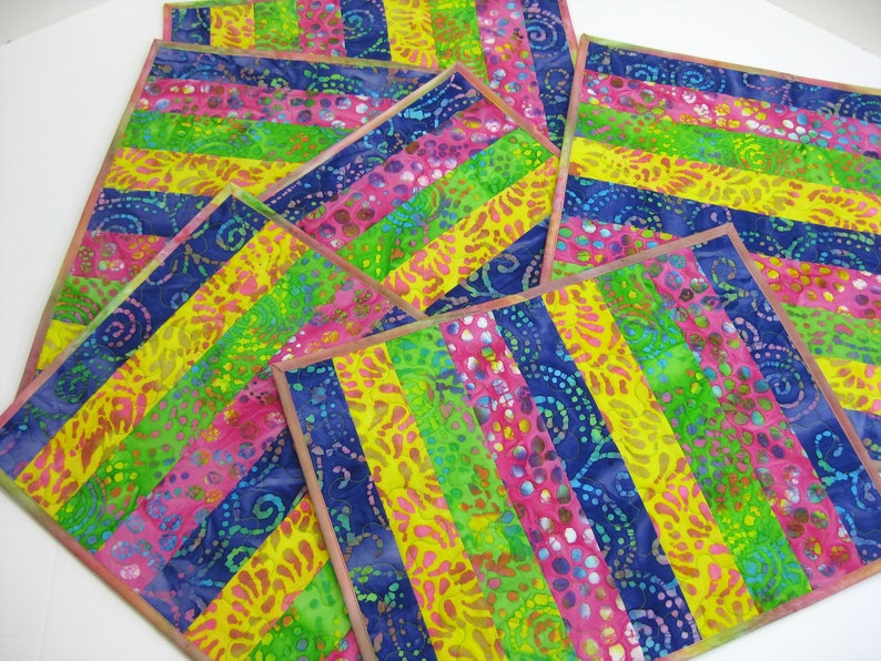 May include: Set of six colorful placemats with a striped pattern in shades of pink, yellow, green, and blue. The placemats are made of fabric with a batik design.
