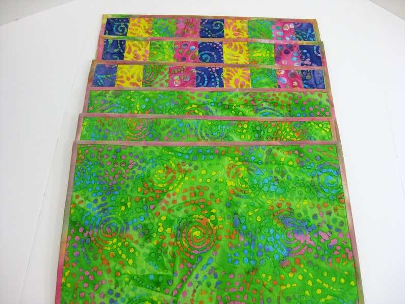 May include: Set of six colorful placemats with a green background and a pattern of swirls and dots. The placemats have a pink border.