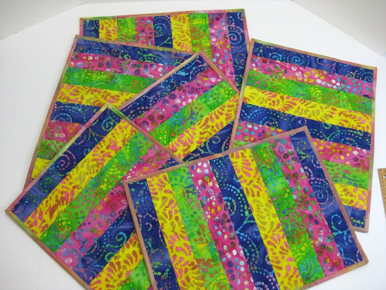 May include: Set of six colorful placemats with a striped pattern in shades of pink, yellow, green, and blue. The fabric has a batik design with swirls and dots.
