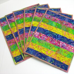 May include: Set of six colorful placemats with a striped pattern in shades of pink, yellow, green, and blue. The placemats are made of fabric with a batik design.