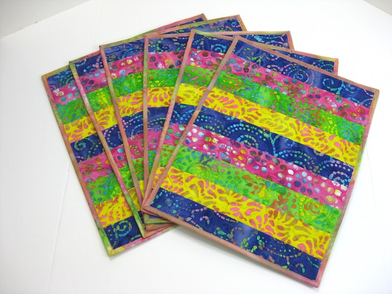 May include: Set of six colorful placemats with a striped pattern in shades of pink, yellow, green, and blue. The placemats are made of fabric with a batik design.