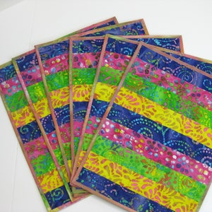 May include: Set of six colorful placemats with a striped pattern. The placemats are made of fabric with a batik design in shades of pink, yellow, green, and blue.