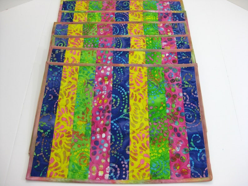 May include: Set of six colorful placemats with a striped pattern in shades of blue, green, yellow, and pink. The placemats are made of fabric with a batik design.