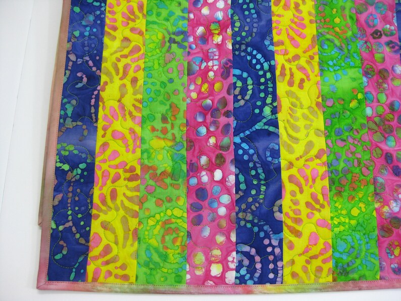 May include: A colorful fabric quilt with vertical stripes in shades of blue, yellow, green, and pink. The fabric has a batik pattern with various shapes and designs.