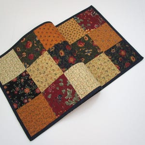 May include: A patchwork quilt with a dark blue border. The quilt is made of squares in various colors, including gold, orange, red, and green, with floral patterns. The quilt is partially folded over.