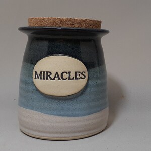 May include: A blue and white ceramic jar with a cork lid. The jar has a label that says "MIRACLES".