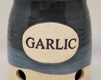 May include: A blue and white ceramic garlic keeper with a cork lid. The keeper has a label that says "GARLIC".