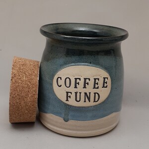 May include: A blue and white ceramic jar with a cork lid. The jar has the words "COFFEE FUND" written on it.