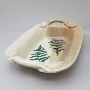 May include: A white ceramic serving dish with a brown and white glaze. The dish has two green fern leaf designs and a sculpted handle.