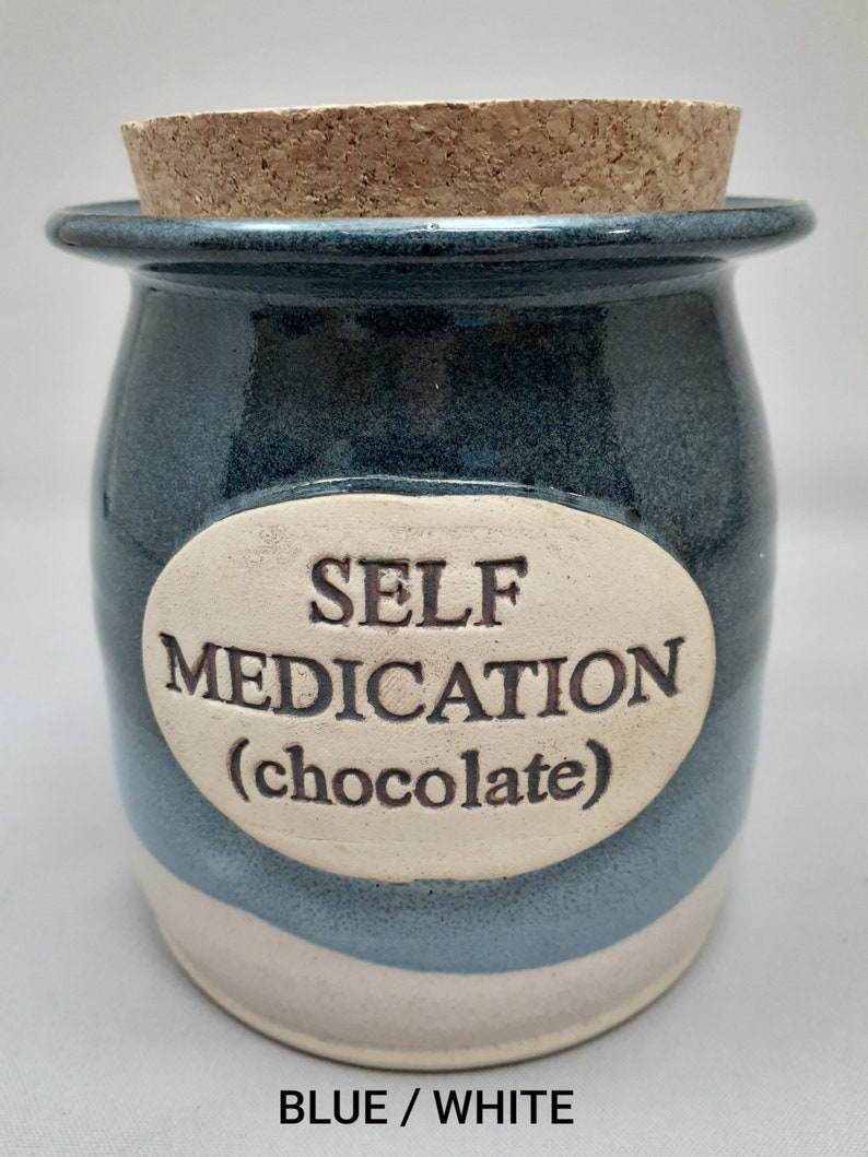 Puede incluir: Un tarro de cer&aacute;mica azul y blanco con tapa de corcho. El tarro tiene una etiqueta ovalada blanca con el texto "SELF MEDICATION (chocolate)".