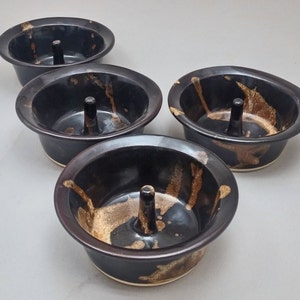 May include: Four black ceramic apple baking dishes with brown glaze. Each dish has a center ring for baking apples.