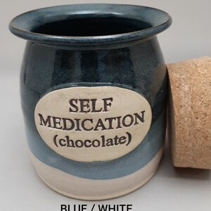 Puede incluir: Tarro de cer&aacute;mica azul y blanco con tapa de corcho. El tarro tiene una etiqueta ovalada blanca con el texto "SELF MEDICATION (chocolate)".