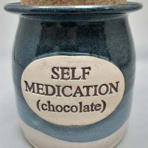Puede incluir: Un tarro de cer&aacute;mica azul y blanco con tapa de corcho. El tarro tiene una etiqueta ovalada blanca con el texto "SELF MEDICATION (chocolate)".