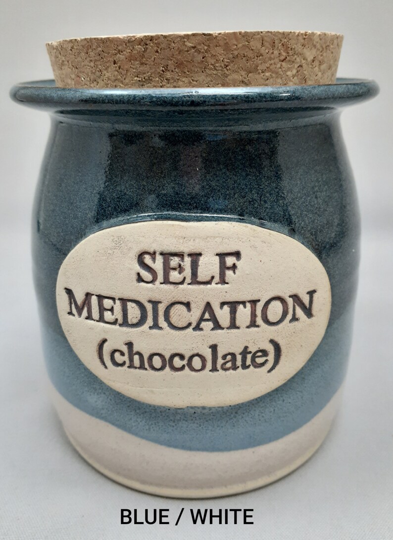 Puede incluir: Un tarro de cer&aacute;mica azul y blanco con tapa de corcho. El tarro tiene una etiqueta ovalada blanca con el texto "SELF MEDICATION (chocolate)".