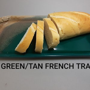 May include: A green and tan ceramic serving tray with a rope-like handle. A loaf of sliced bread is on the tray. GREEN/TAN FRENCH TRAY