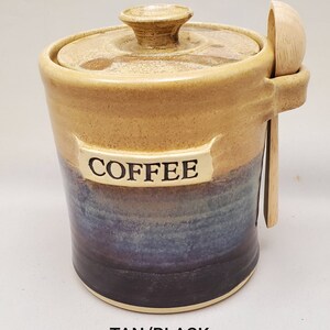 May include: Tan and black ceramic coffee jar with a wooden spoon. The jar has a lid and says "COFFEE" on the front.