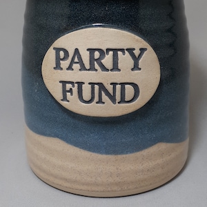 May include: A blue and white ceramic jar with a cork lid. The jar has a white oval label with the text "PARTY FUND" in black lettering.
