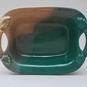 May include: A green and brown ceramic serving dish with two leaf-shaped handles. The dish has a speckled glaze and is perfect for serving snacks or appetizers.