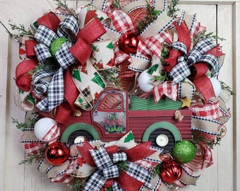 May include: A red and green Christmas wreath with a red truck in the center. The wreath is decorated with red and white buffalo plaid ribbon, green and white plaid ribbon, red and white gingham ribbon, and white and green ornaments.