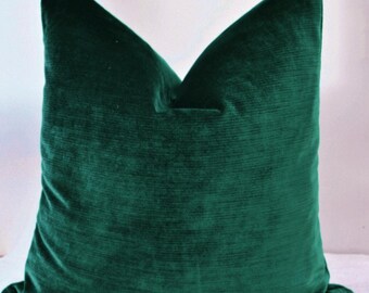 May include: A plush, emerald green pillow with a soft, velvety texture. The pillow has a classic square shape and a subtle ribbed pattern, adding depth and visual interest. The rich color and luxurious feel make it a stylish accent for any room.