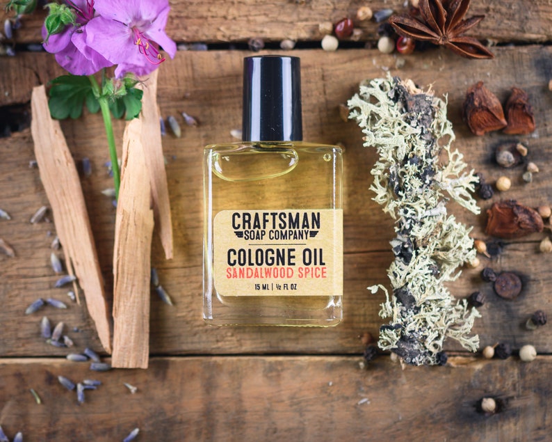 May include: A clear glass bottle of sandalwood spice cologne oil with a black cap. The bottle is labeled "Craftsman Soap Company Cologne Oil Sandalwood Spice 15 ml | 1/2 fl oz".