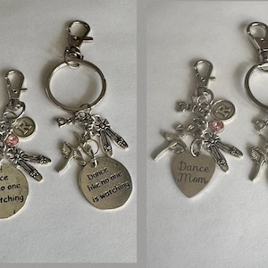 May include: Silver keychains with dance-themed charms. One keychain has a round charm with the text "Dance like no one is watching." The other keychain has a heart-shaped charm with "Dance Mom." Both have ballet shoe and bird charms.