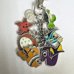 May include: A silver-tone keychain featuring colorful enamel charms of sea creatures. The charms include a starfish, turtle, clownfish, and other fish. The keychain has a lobster clasp for easy attachment to bags or keys.