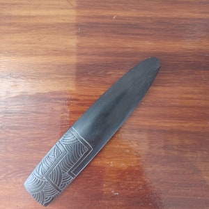 May include: A black wooden carving with a geometric pattern. The carving is on a wooden surface.