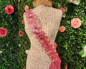 May include: Pink satin sash with gold glitter lettering that reads "Birthday Queen".