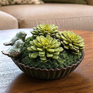 May include: A dark brown fluted ceramic bowl filled with green moss, three artificial succulent plants, and two small light blue ceramic birds with brown wing details. The birds are positioned on the edge of the bowl next to the moss and plants.