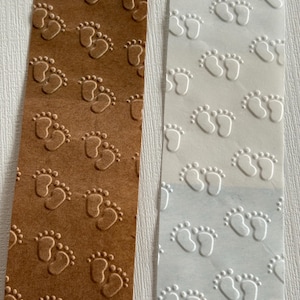May include: Two rectangular paper tags, one brown and one white, are embossed with a pattern of tiny footprints. The brown tag has a warm, earthy tone, while the white tag has a clean, crisp appearance. The footprints are evenly spaced.