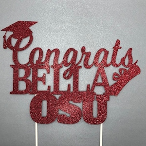 May include: Red glitter cake topper with the text "Congrats Bella OSU" and a graduation cap.
