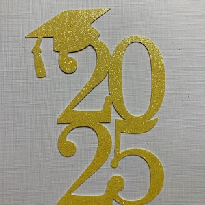 May include: Glittery gold graduation cap and the numbers 2025, cut from a textured material. The cap is positioned above the number 2, with the tassel hanging down. The numbers are stacked vertically, with the 20 on top and the 25 below.