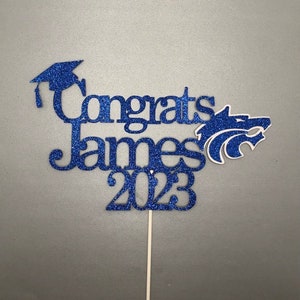 May include: Blue glitter graduation cake topper with a graduation cap, the name "James", and the year "2023".