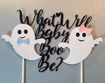 Può includere: Un topper per torta con due fantasmi bianchi, uno con un fiocco blu e l'altro con un fiocco rosa. Il testo "What will Baby Boo Be?" è scritto in glitter nero.