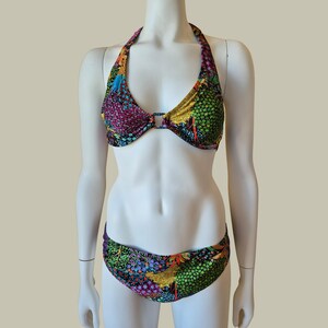 Puede incluir: Un conjunto de bikini de dos piezas con un vibrante estampado floral y de estrellas multicolor. La parte superior de estilo halter incluye un detalle de anillo central que conecta las copas, mientras que la braga de bikini de tiro bajo completa el conjunto.