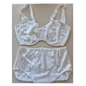 May include: A white lingerie set featuring a bra and high-waisted briefs. The bra has adjustable straps and decorative lace trim along the cups and neckline. The briefs have matching lace detailing. The set is made of a smooth, satin-like fabric.