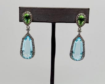 Peut inclure: Une paire de boucles d'oreilles pendantes avec une pierre de topaze bleue en forme de larme entourée d'un halo de petits diamants. Le haut de la boucle d'oreille présente une pierre de péridot verte en forme de poire également entourée d'un halo de petits diamants.