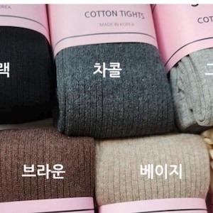 May include: Eight pairs of cotton tights in different colors, including black, gray, beige, brown, cream, and purple. The tights are ribbed and have the words "Cotton Tights" and "Made in Korea" printed on the packaging. The Korean words for each color are also printed on the packaging.
