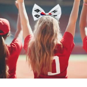 May include: Image of people wearing red shirts and a headband with the South Korean flag, cheering with their arms raised. The image has Korean text at the top and bottom.