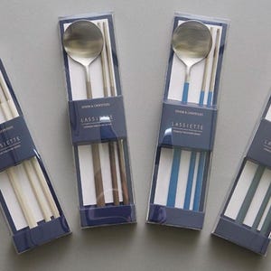 Può includere: Quattro set di bacchette e cucchiai d'argento confezionati in scatole di plastica trasparente con etichette blu e bianche. Le etichette riportano "Spoon & Chopsticks" e "Lassiette".