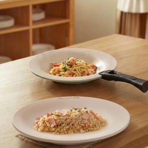 Puede incluir: Dos platos de cer&aacute;mica con comida sobre una mesa de madera. Uno contiene espaguetis con gambas y el otro arroz frito. El plato superior tiene un asa negra. Los platos son de color blanquecino con una textura moteada.